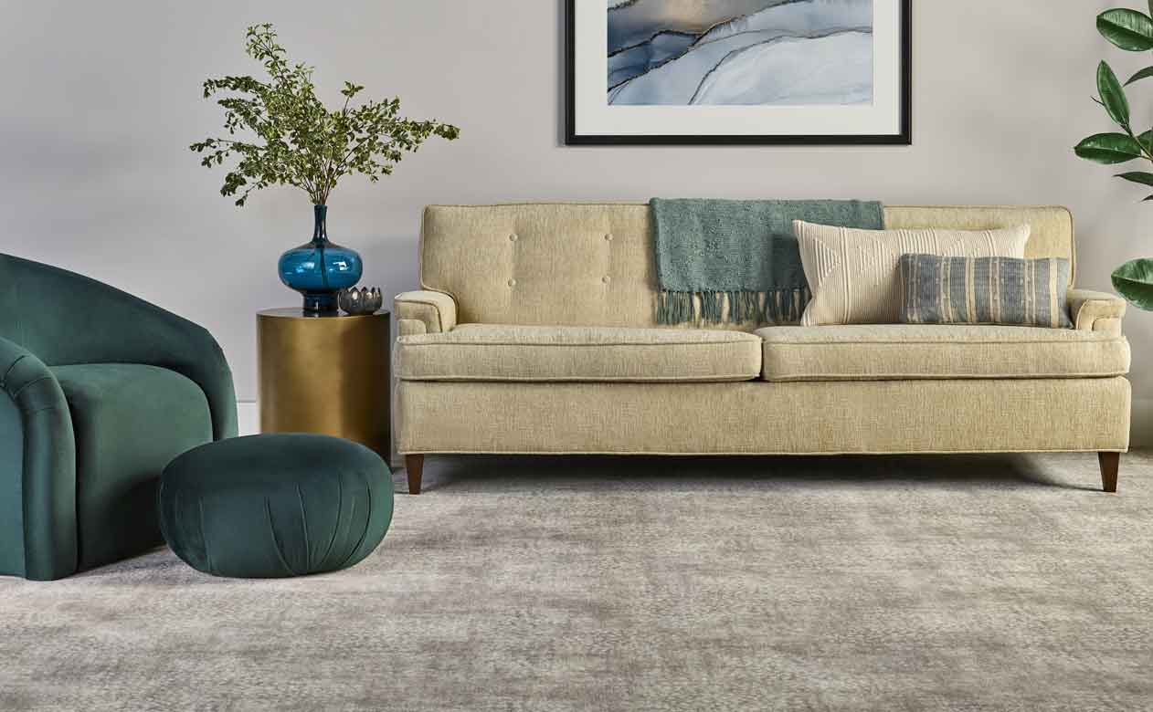 Greige patterned rug in modern living room with velvet green chair and ottoman, beige couch and gold table end
